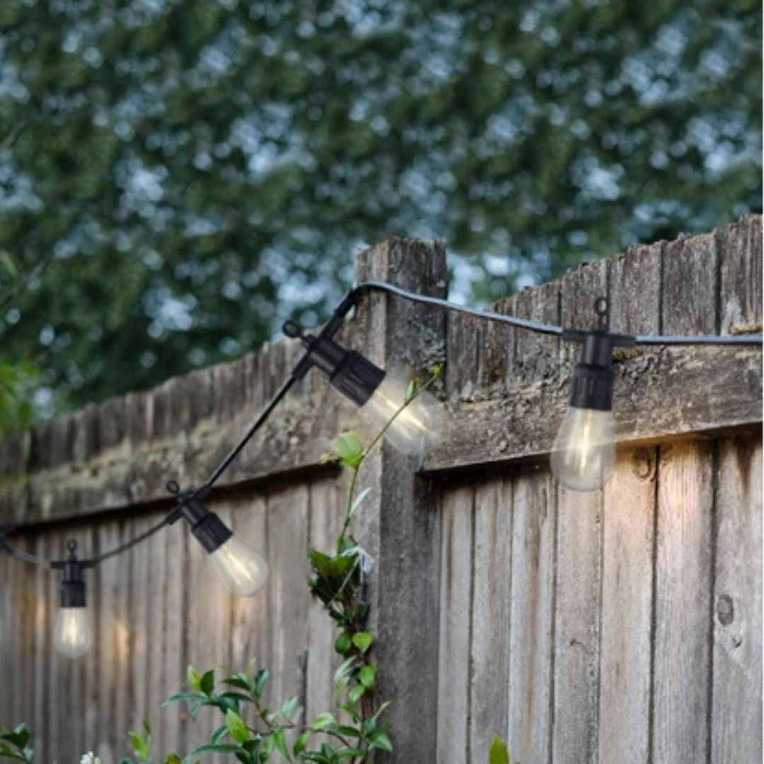 Catena luminosa da esterno con lampadine LED fissata a una staccionata in legno al tramonto