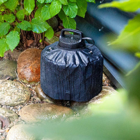 Cappuccio protettivo nero per Geyser 4L installato all’esterno su fondo roccioso, circondato da piante