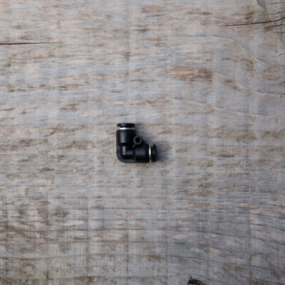 Raccordo angolare a 90 gradi per tubo Geyser System da 6 mm, posato su superficie in legno naturale