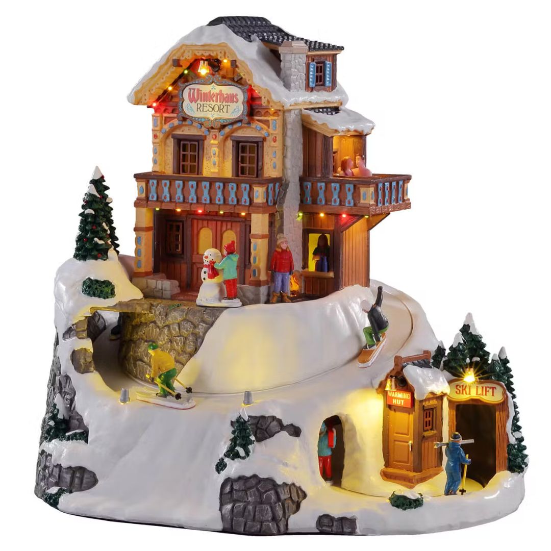 Villaggio natalizio Lemax Winterhaus Resort illuminato, con chalet innevato, sciatori, snowborder e impianto di risalita.