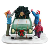Famiglia che carica un albero di Natale sul tetto di un'auto verde parcheggiata su base innevata vista frontalmente.