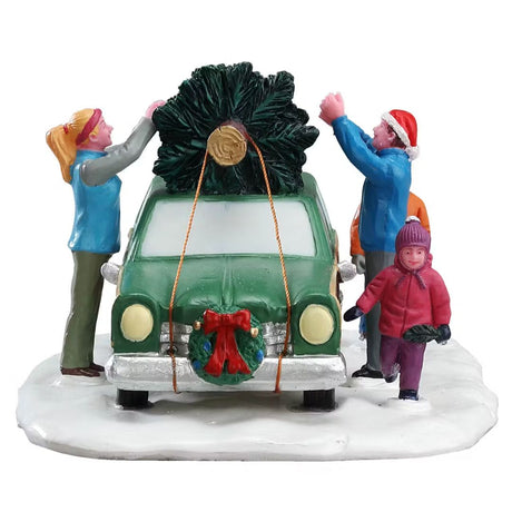 Famiglia che carica un albero di Natale sul tetto di un'auto verde parcheggiata su base innevata vista frontalmente.