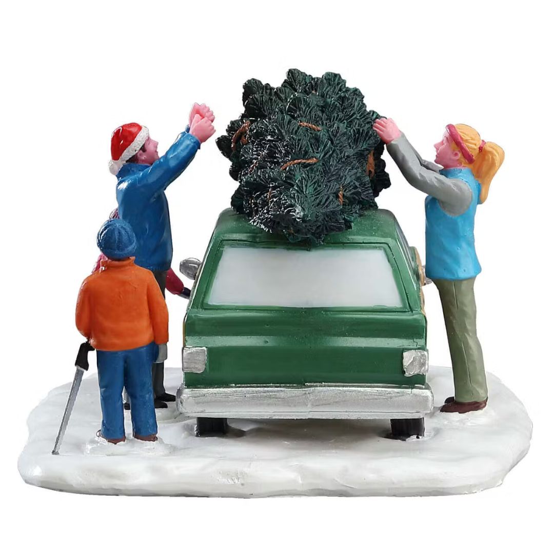 Famiglia che carica un albero di Natale sul tetto di un'auto verde parcheggiata su base innevata vista dal retro.