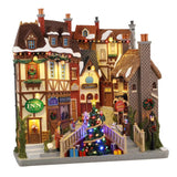 Facciata natalizia in stile inglese con locanda, pub, libreria e al centro un albero di Natale illuminato con pacchi regalo.