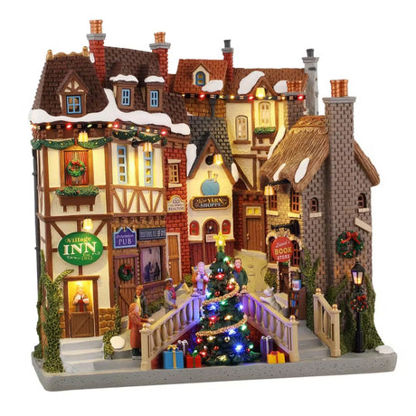 Facciata natalizia in stile inglese con locanda, pub, libreria e al centro un albero di Natale illuminato con pacchi regalo.