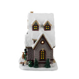 Retro della casetta natalizia con finestre illuminate, doppio abbaino sul tetto e decorazioni natalizie su base innevata.