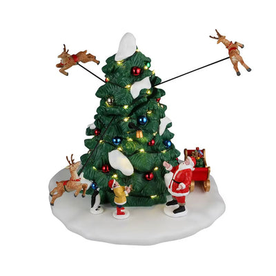 Albero di Natale con luci e decorazioni, Babbo Natale alla base con bambini e slitta, renne sospese in volo intorno all’albero.