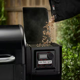Dettaglio del serbatoio laterale del barbecue Weber Smoque durante il caricamento dei pellet