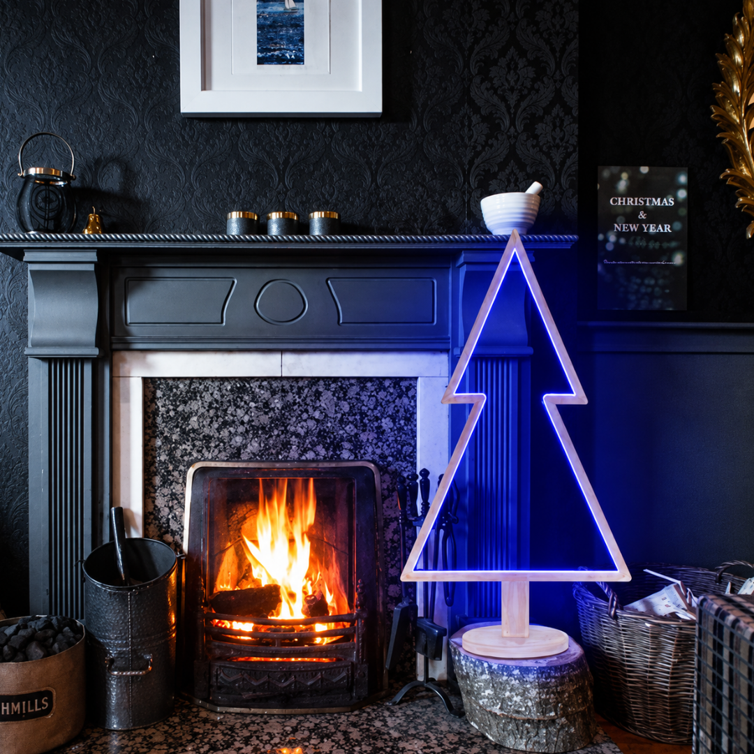 Albero di Natale in legno sbiancato con illuminazione LED blu, posizionato accanto a un camino acceso.