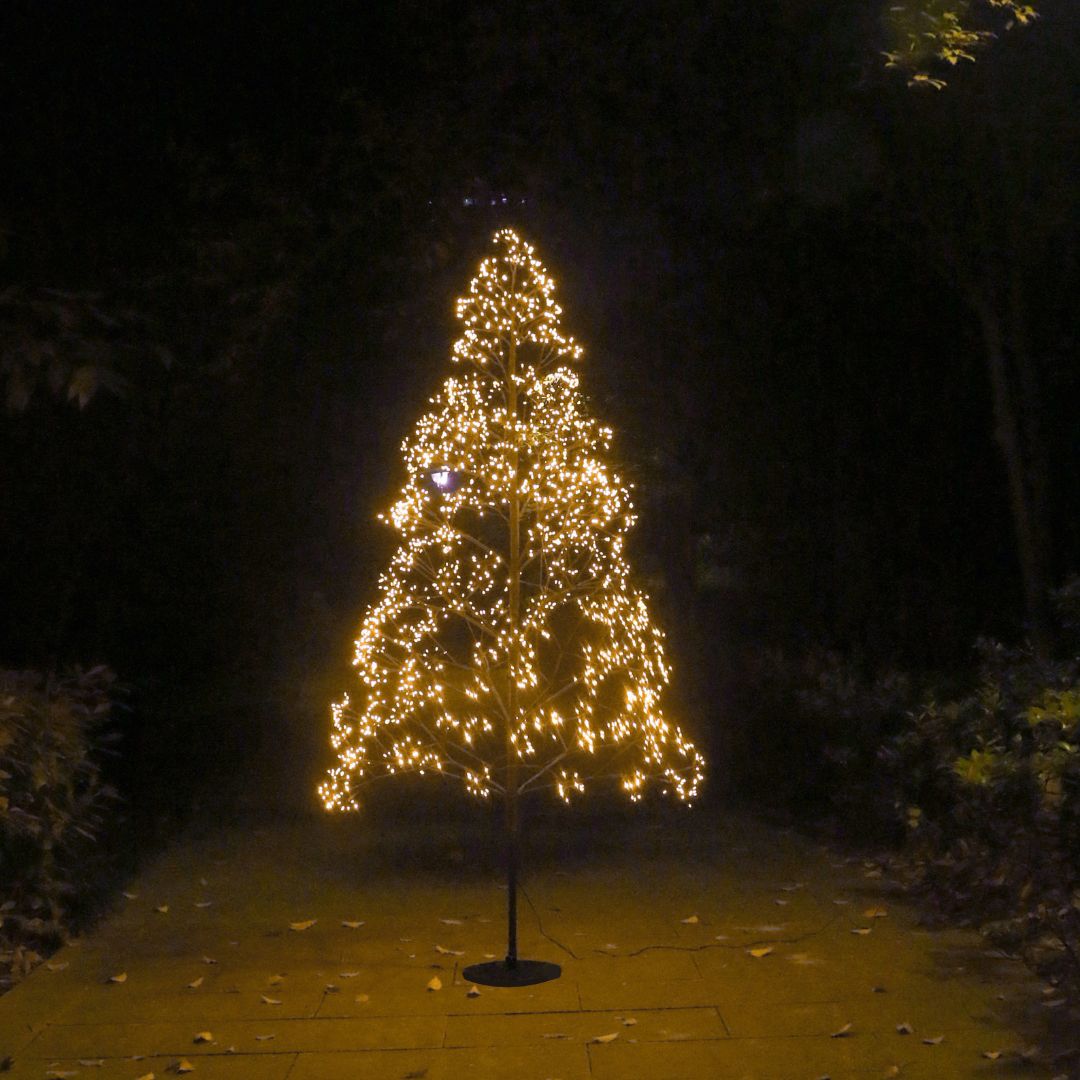 Albero decorativo alto 180 cm a LED bianco caldo acceso di notte con luci distribuite a ciuffi.