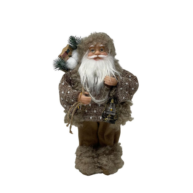 Figura decorativa di Babbo Natale in abiti beige con maglione lavorato, barba bianca, lanterna in mano e sacco con rami e pacchi regalo, alto 30cm. 