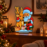 Decorazione luminosa con Babbo Natale e renna ambientata in casa su un mobile, con luci calde e atmosfera festiva