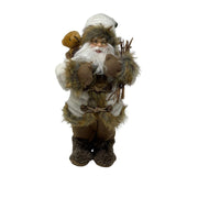 Figura decorativa di Babbo Natale in abiti invernali beige e marroni, con occhiali, barba bianca, sacco con orsacchiotto e fascina di rami in mano, alto 30cm.