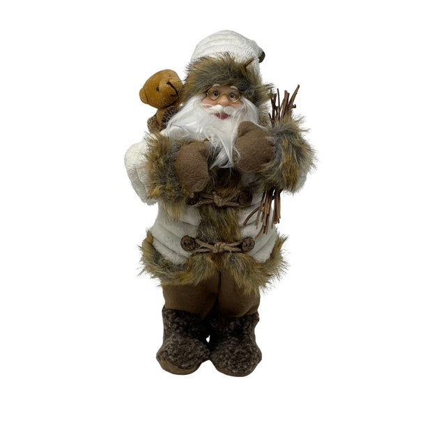 Figura decorativa di Babbo Natale in abiti invernali beige e marroni, con occhiali, barba bianca, sacco con orsacchiotto e fascina di rami in mano, alto 30cm.