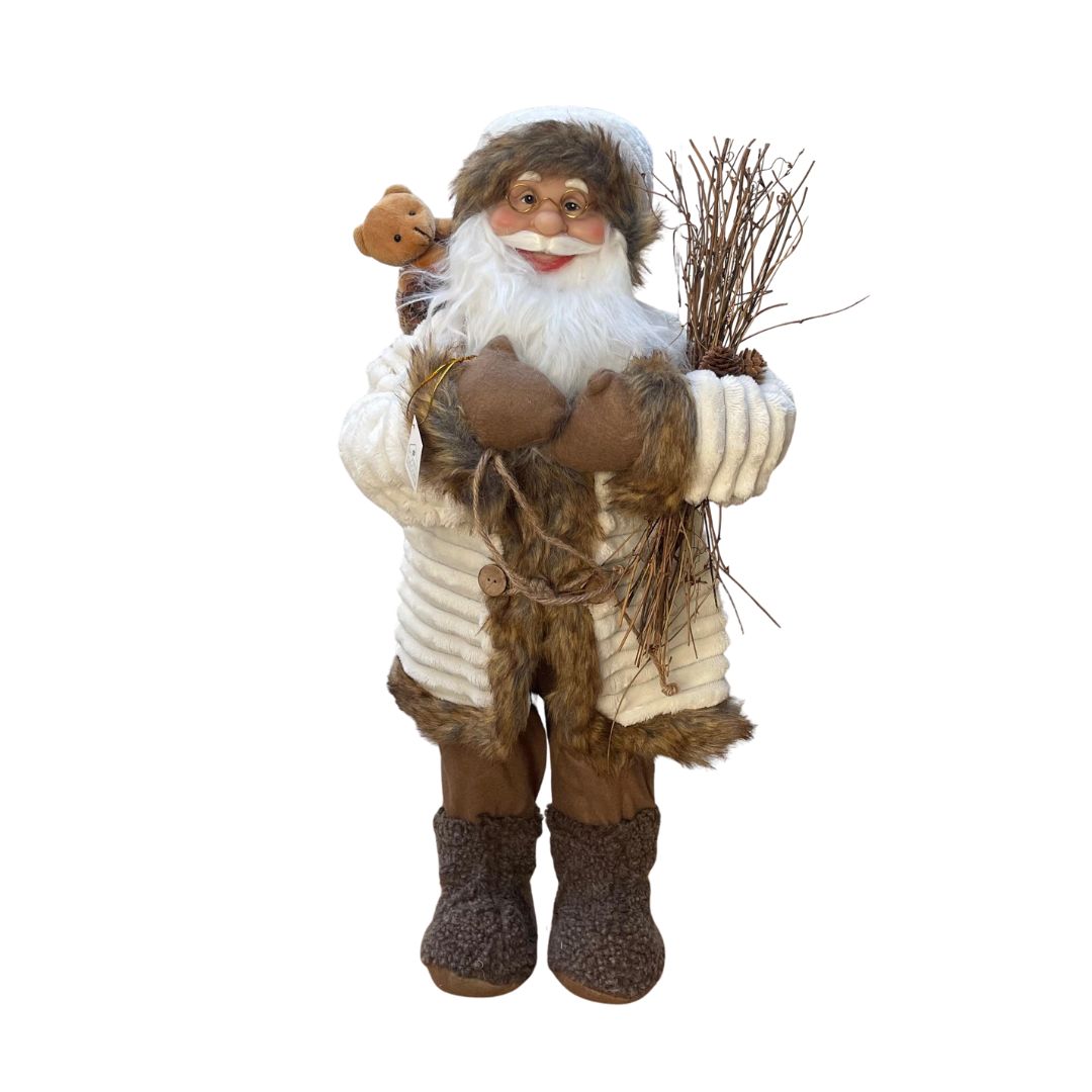 Figura decorativa di Babbo Natale in abiti invernali beige e marroni, con occhiali, barba bianca, sacco con orsacchiotto e fascina di rami in mano, alto 60cm.