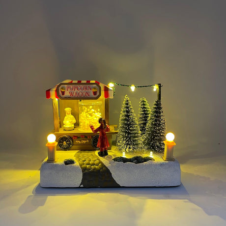 Miniatura natalizia con bancarella Popcorn Wagon, personaggio in cappotto rosso e alberi innevati decorativi e luci LED accese.