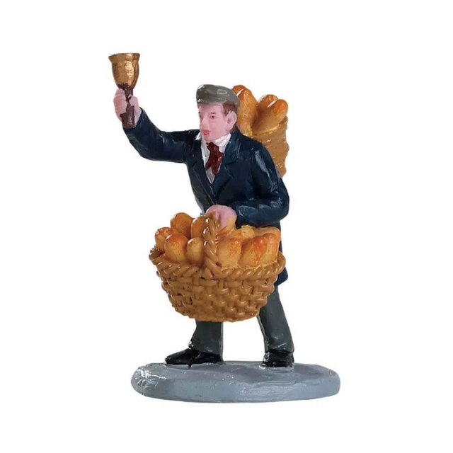 Venditore di pane Lemax con cesta piena di pagnotte e baguette, mentre alza una campanella per richiamare i clienti.