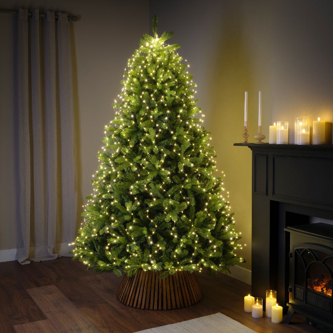 Albero natalizio decorato con micro LED bianco caldo accanto a caminetto e candele.