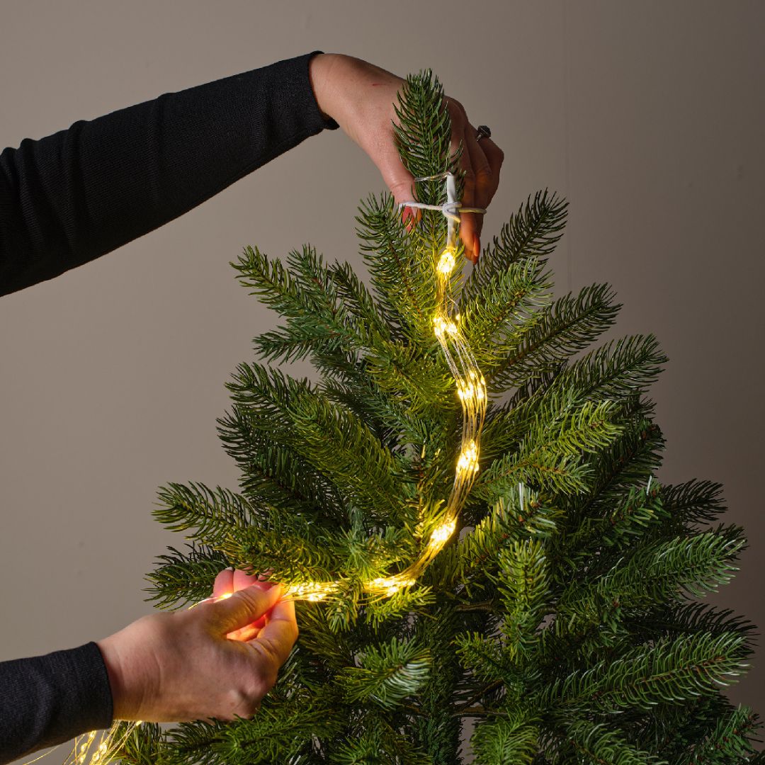 Mani che fissano l'elastico bianco delle luci LED sulla punta dell’albero di Natale.