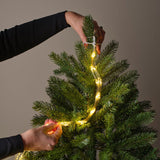 Mani che fissano l'elastico bianco delle luci LED sulla punta dell’albero di Natale.
