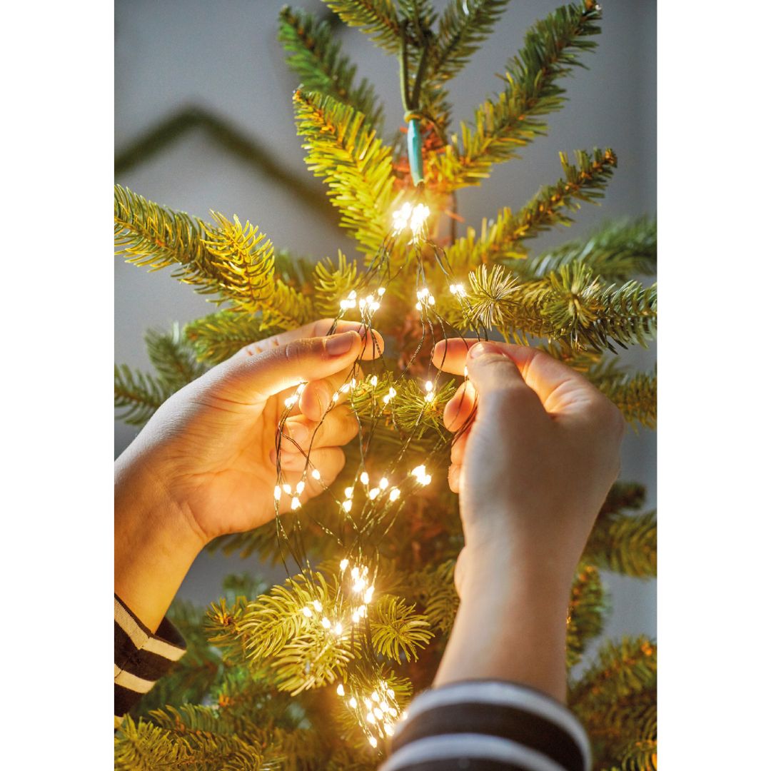 Mani che sistemano fili di luci LED calde tra i rami di un albero di Natale.