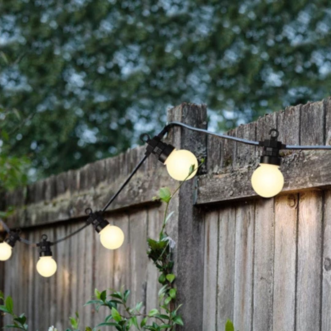 Catena LED con luce bianca calda installata su staccionata in legno in un giardino al tramonto