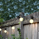 Catena LED con luce bianca calda installata su staccionata in legno in un giardino al tramonto