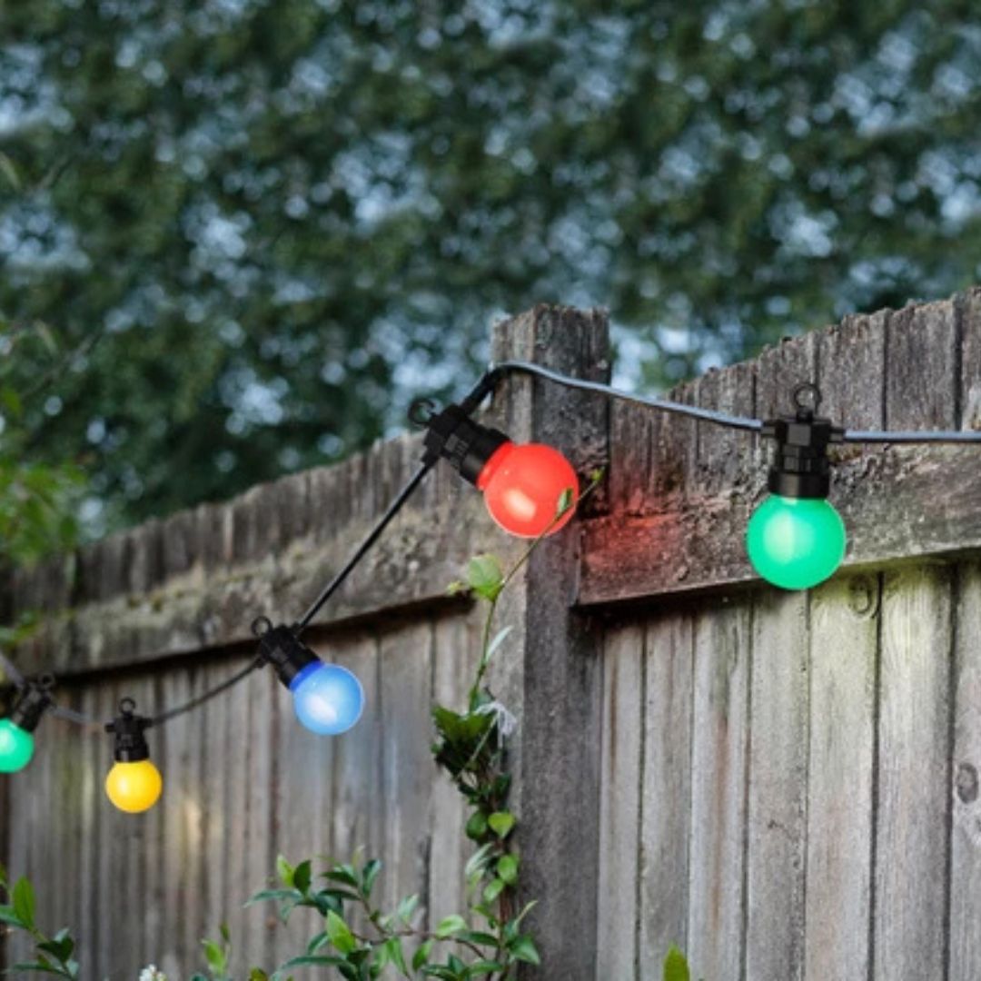 Catena di luci multicolore appesa a una staccionata in legno, accesa in un giardino verde