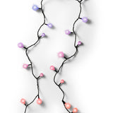 Primo piano di una catena di luci LED multicolore con palline rosa, lilla e viola su sfondo bianco.