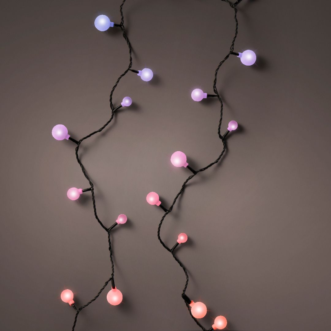 Primo piano di una catena di luci LED multicolore con palline rosa, lilla e viola su sfondo scuro.