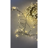 Filo cluster con 500 micro LED a luce calda su cavo verde, acceso e disposto su superficie chiara.