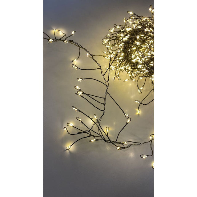 Filo cluster con 500 micro LED a luce calda su cavo verde, acceso e disposto su superficie chiara.