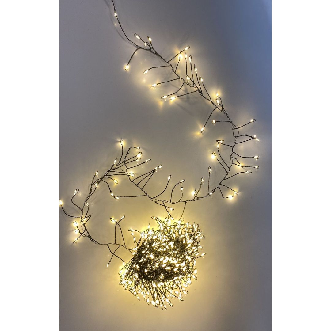 Filo cluster con 500 micro LED a luce calda su cavo verde, acceso e disposto su superficie chiara.