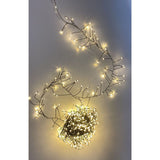 Filo cluster con 500 micro LED a luce calda su cavo verde, acceso e disposto su superficie chiara.