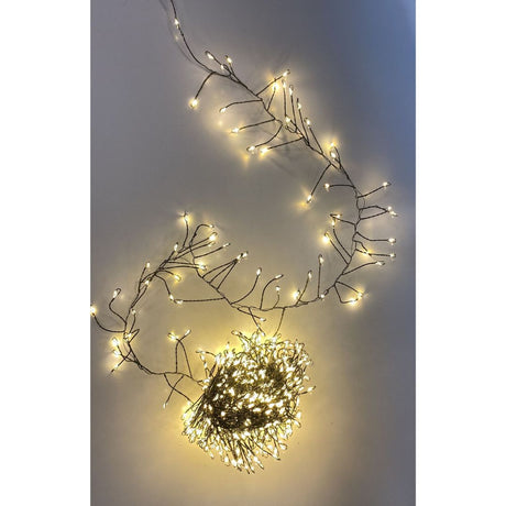 Filo cluster con 500 micro LED a luce calda su cavo verde, acceso e disposto su superficie chiara.