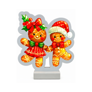 Decorazione luminosa natalizia con coppia di omini di pan di zenzero, uno con cappello di Babbo Natale e l’altra con fiocco rosso e agrifoglio