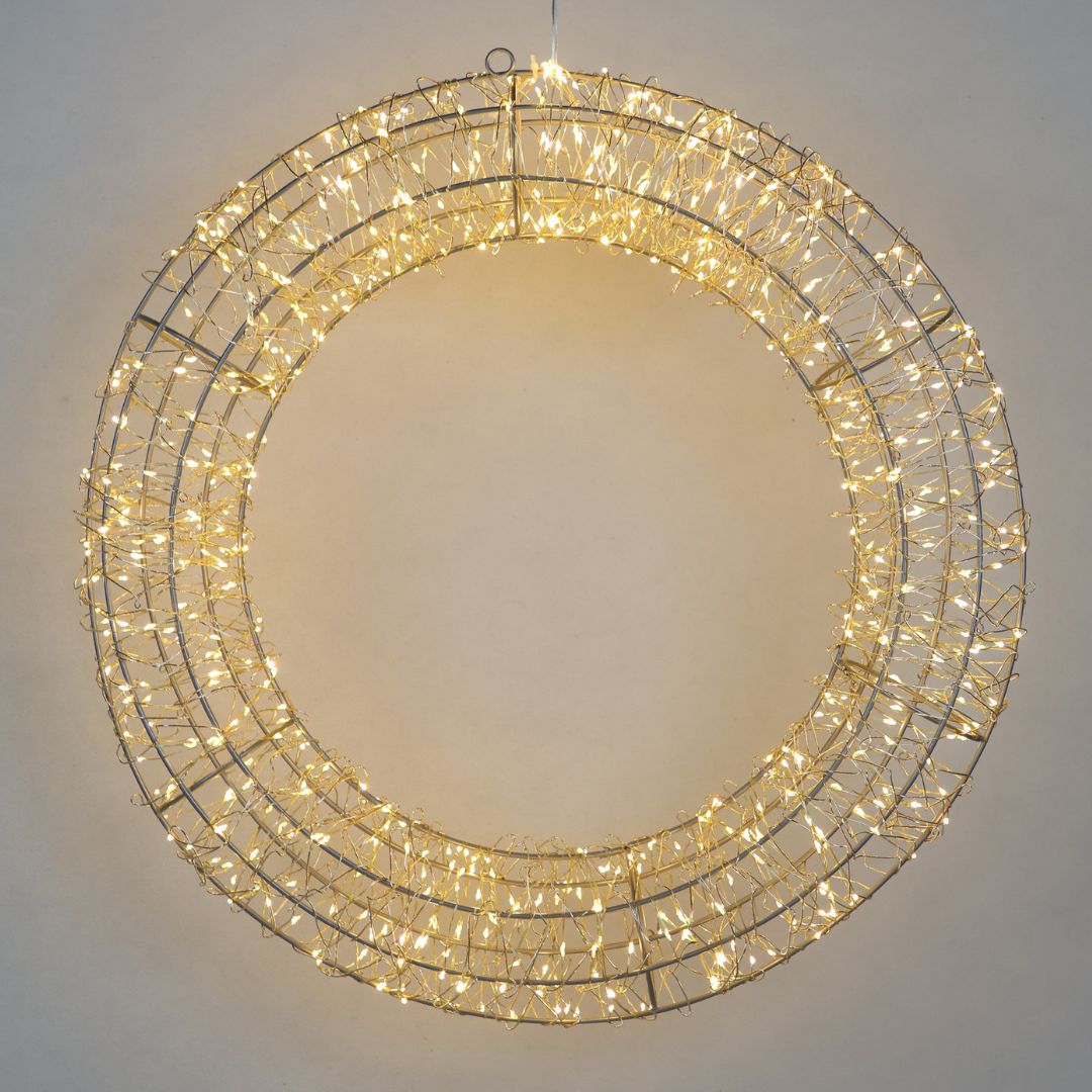 Corona luminosa decorativa a LED di colore bianco caldo, con struttura metallica circolare intrecciata con diametro 38cm su parete grigia.