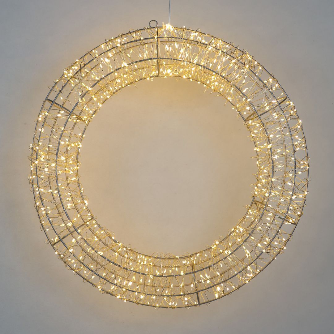 Corona luminosa decorativa a LED di colore bianco caldo, con struttura metallica circolare intrecciata con diametro 58cm su parete grigia.