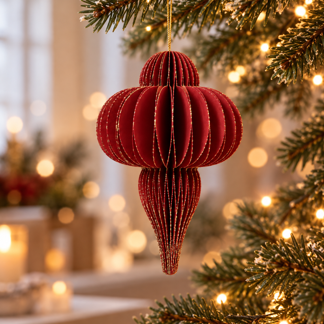 Decorazione natalizia rossa in carta pieghettata appesa all’albero di Natale tra luci calde