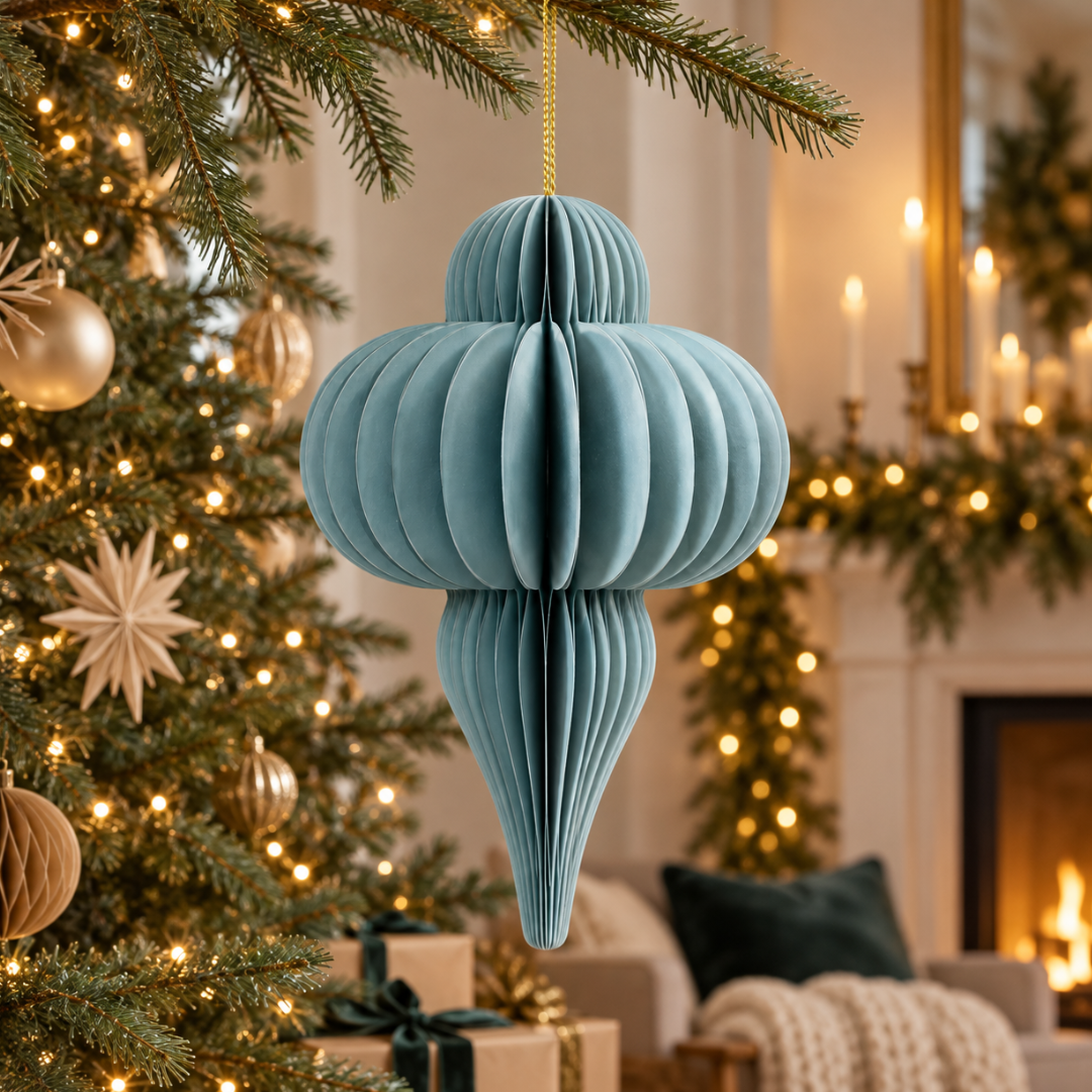 Decorazione natalizia sospesa in carta azzurra pieghettata, appesa a un ramo dell’albero di Natale in un ambiente festivo