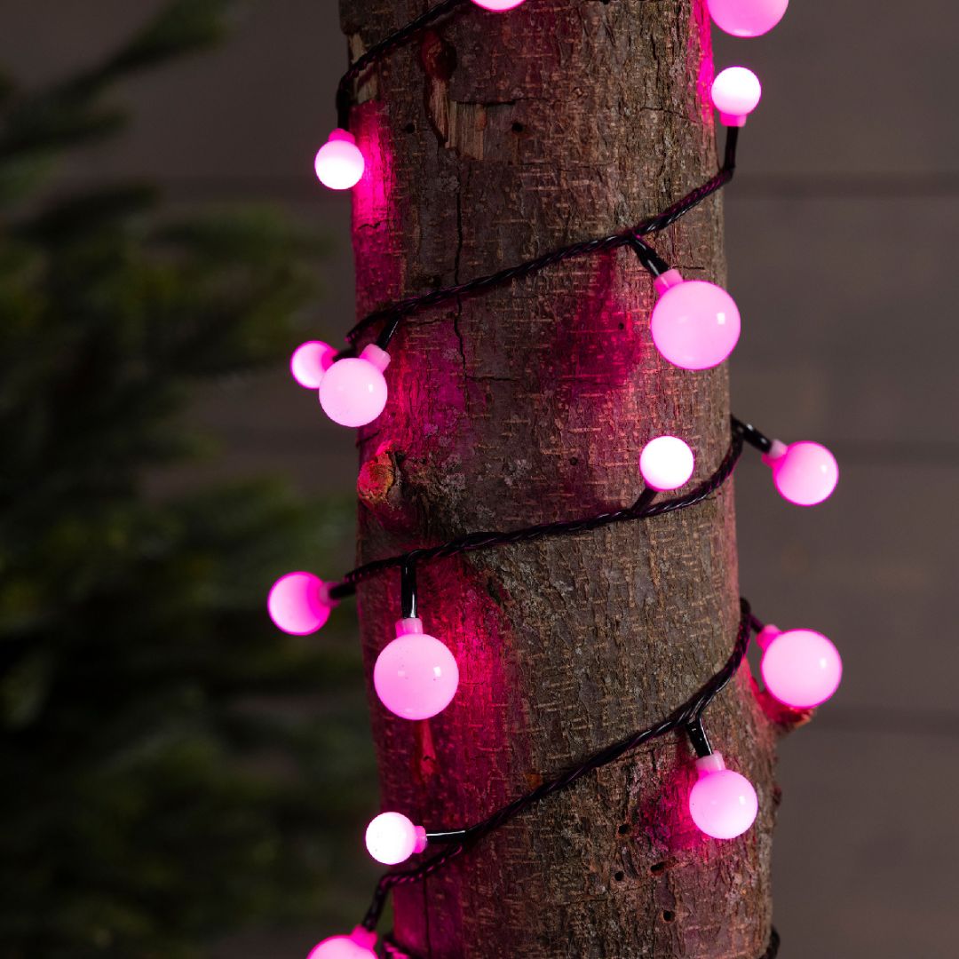 Luci LED multicolore a forma di ciliegia, avvolte attorno al tronco di un albero, illuminate di color rosa.