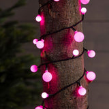 Luci LED multicolore a forma di ciliegia, avvolte attorno al tronco di un albero, illuminate di color rosa.