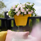 Fioriera da balcone Elho colore giallo con fiori rosa fissata alla ringhiera.