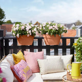 Fioriera da balcone Elho con fiori rosa installata su ringhiera sopra divanetto da esterno.