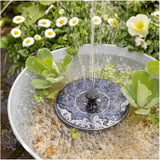 Fontana solare galleggiante in funzione in un catino metallico tra fiori e piante verdi