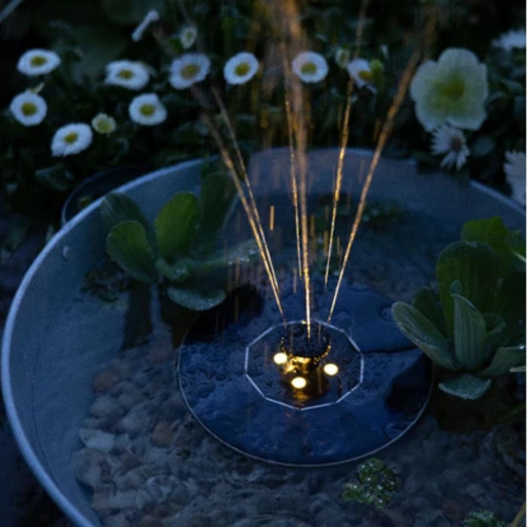 Fontana solare in funzione con luci LED accese di notte, immersa in un giardino