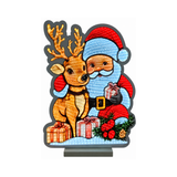 Decorazione luminosa con Babbo Natale accanto a una renna, pacchi regalo e rami natalizi con bacche rosse