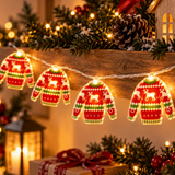 Catena luminosa con maglioncini rossi decorati con renne ambientata tra addobbi natalizi