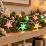 Catena luminosa con stelle multicolore tra rami verdi e decorazioni natalizie
