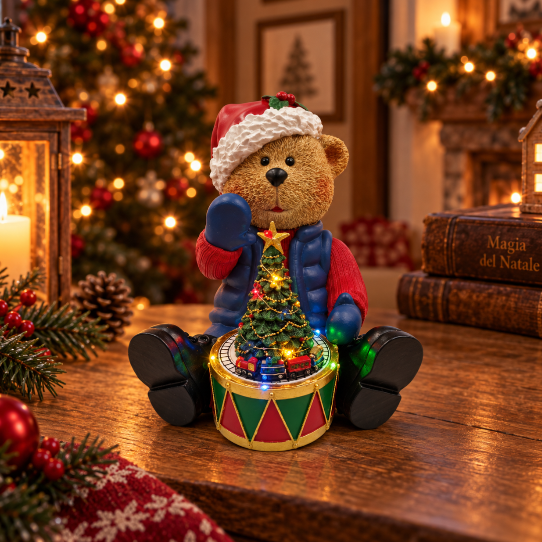 Orsetto natalizio con cappello di Babbo Natale e albero illuminato con trenino, ambientato su un tavolo con decorazioni di Natale